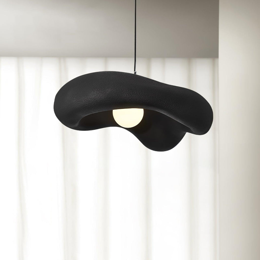 Black Clérachic pendant with a rough, wavy shade and a round bulb, hung in front of sheer white curtains.