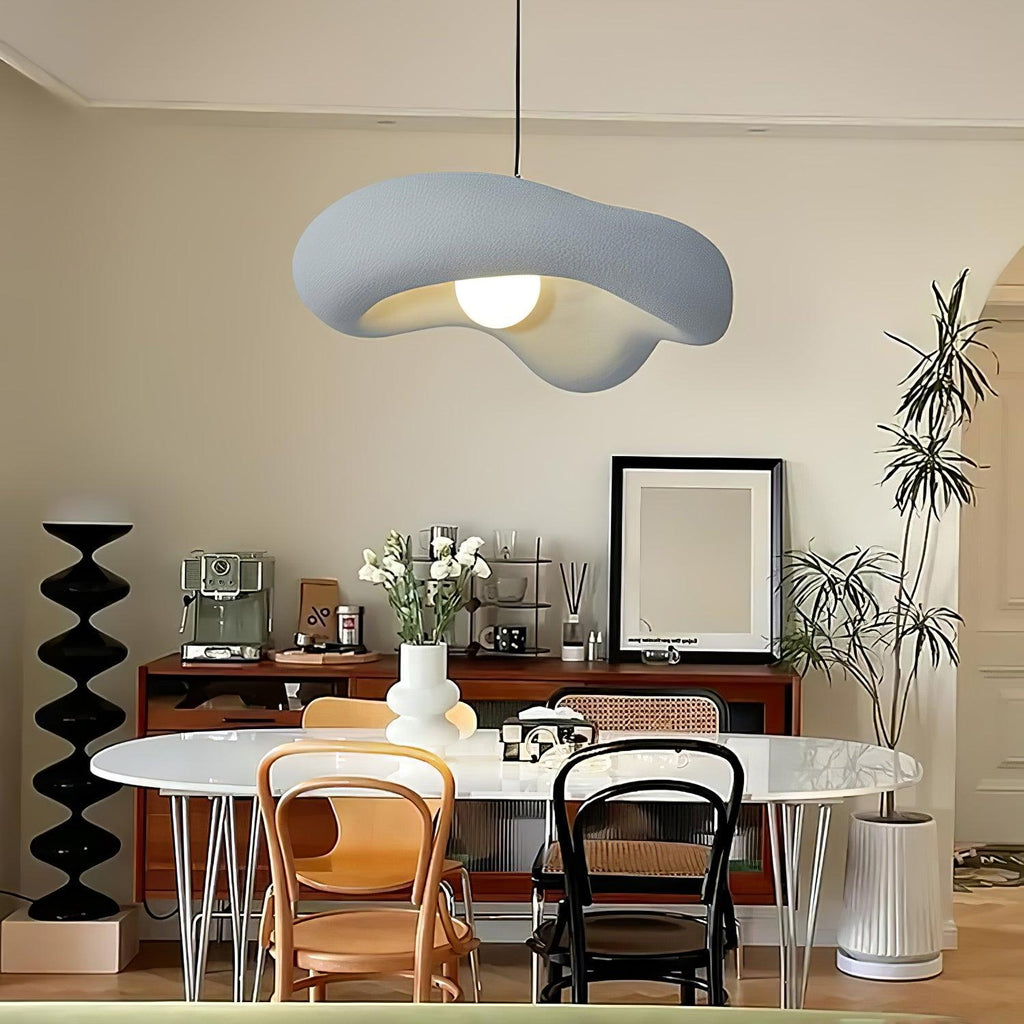 Grey Clérachic pendant with a soft wavy shade over a round white dining table with bentwood chairs and a black sculptural stand.
