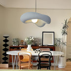 Grey Clérachic pendant with a soft wavy shade over a round white dining table with bentwood chairs and a black sculptural stand.