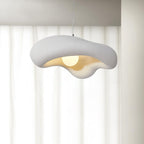 White Clérachic pendant with a rippled, rough-textured shade and a glowing bulb, against sheer white curtains.