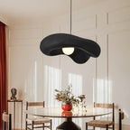 Black Clérachic pendant above a round glass dining table with rush-seat chairs, in a room with panelled walls and red curtains.