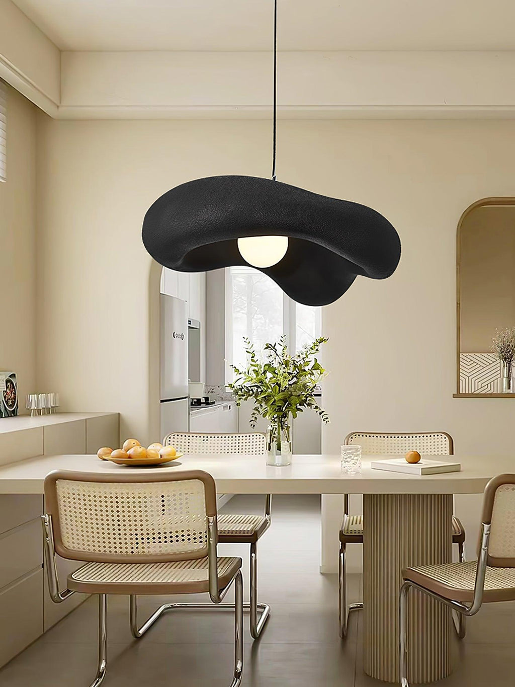 Black Clérachic pendant over a pale curved dining table with rattan chairs, a vase of greenery and an arched alcove behind.