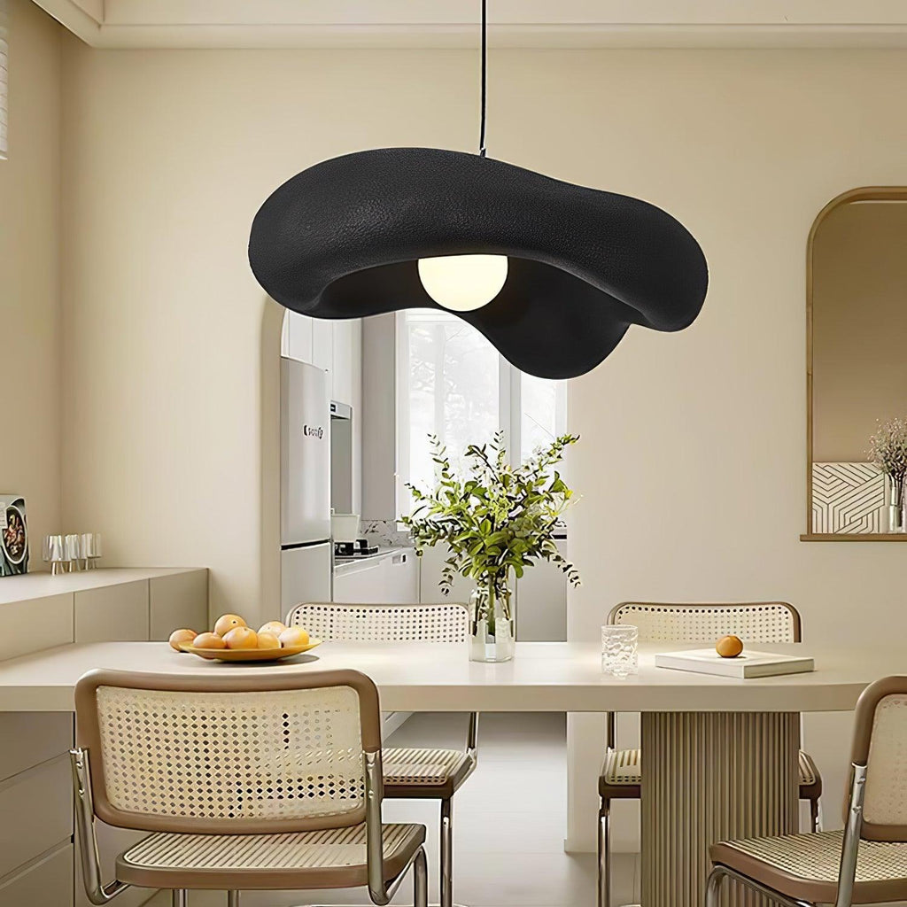 Closer view of a black Clérachic pendant over a dining table with cane chairs, fruit and a vase of green stems.