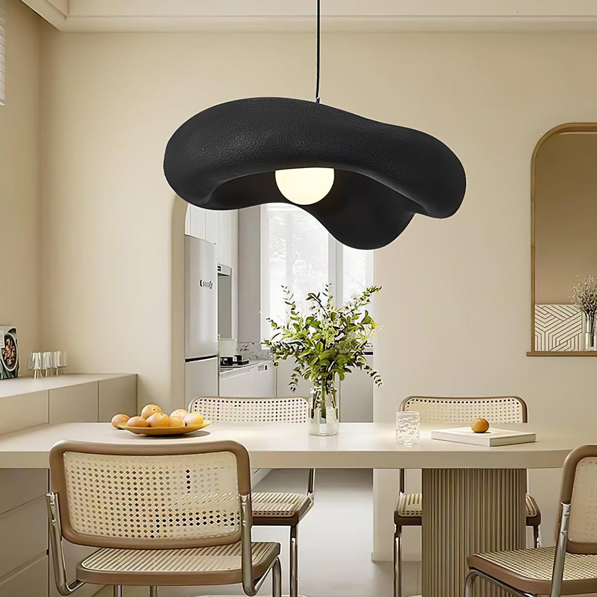 Closer view of a black Clérachic pendant over a dining table with cane chairs, fruit and a vase of green stems.