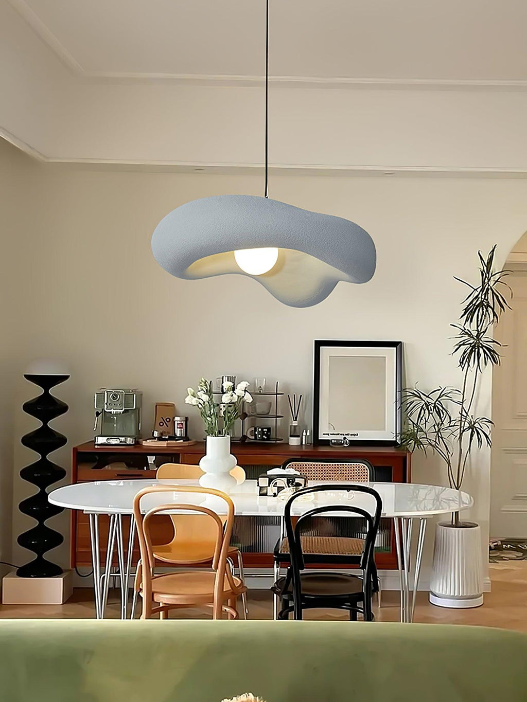 Grey Clérachic pendant above an oval white table with bentwood chairs, a dark sideboard and a potted plant behind.