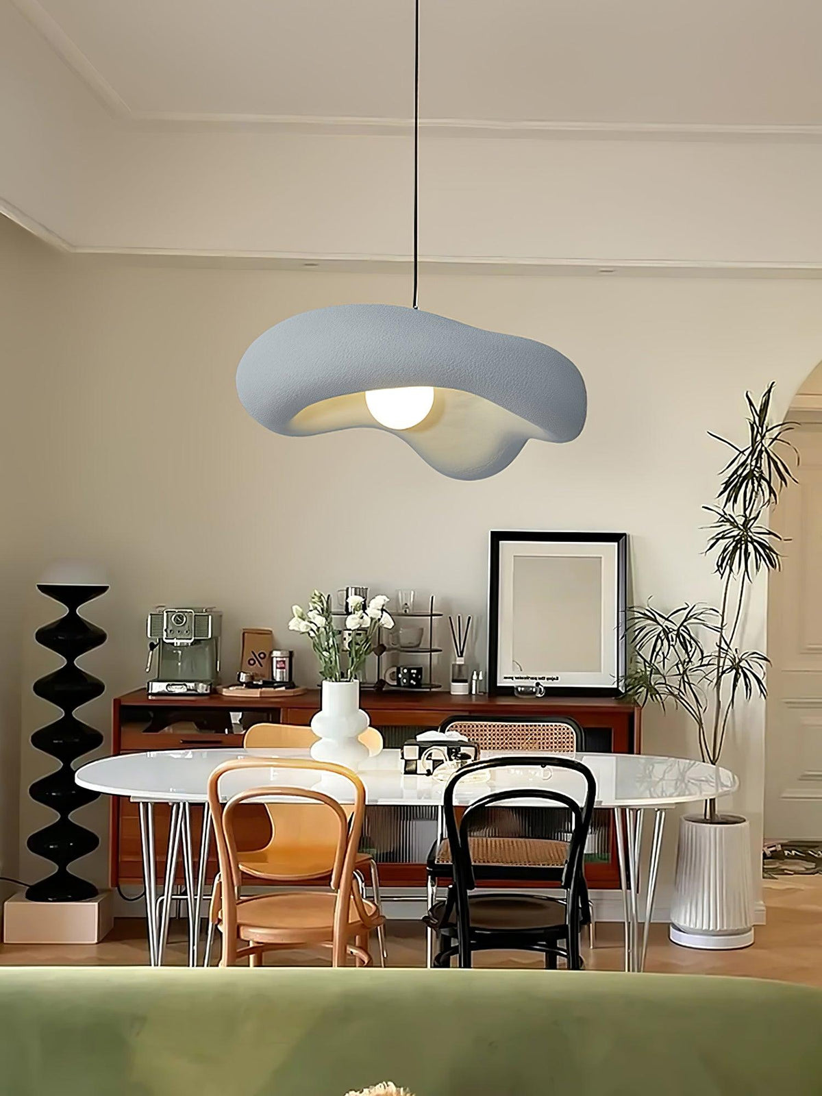 Grey Clérachic pendant above an oval white table with bentwood chairs, a dark sideboard and a potted plant behind.