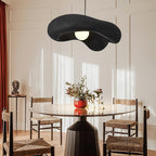Black Clérachic pendant hung high in a panelled room, above a round glass table and rush-seat chairs.
