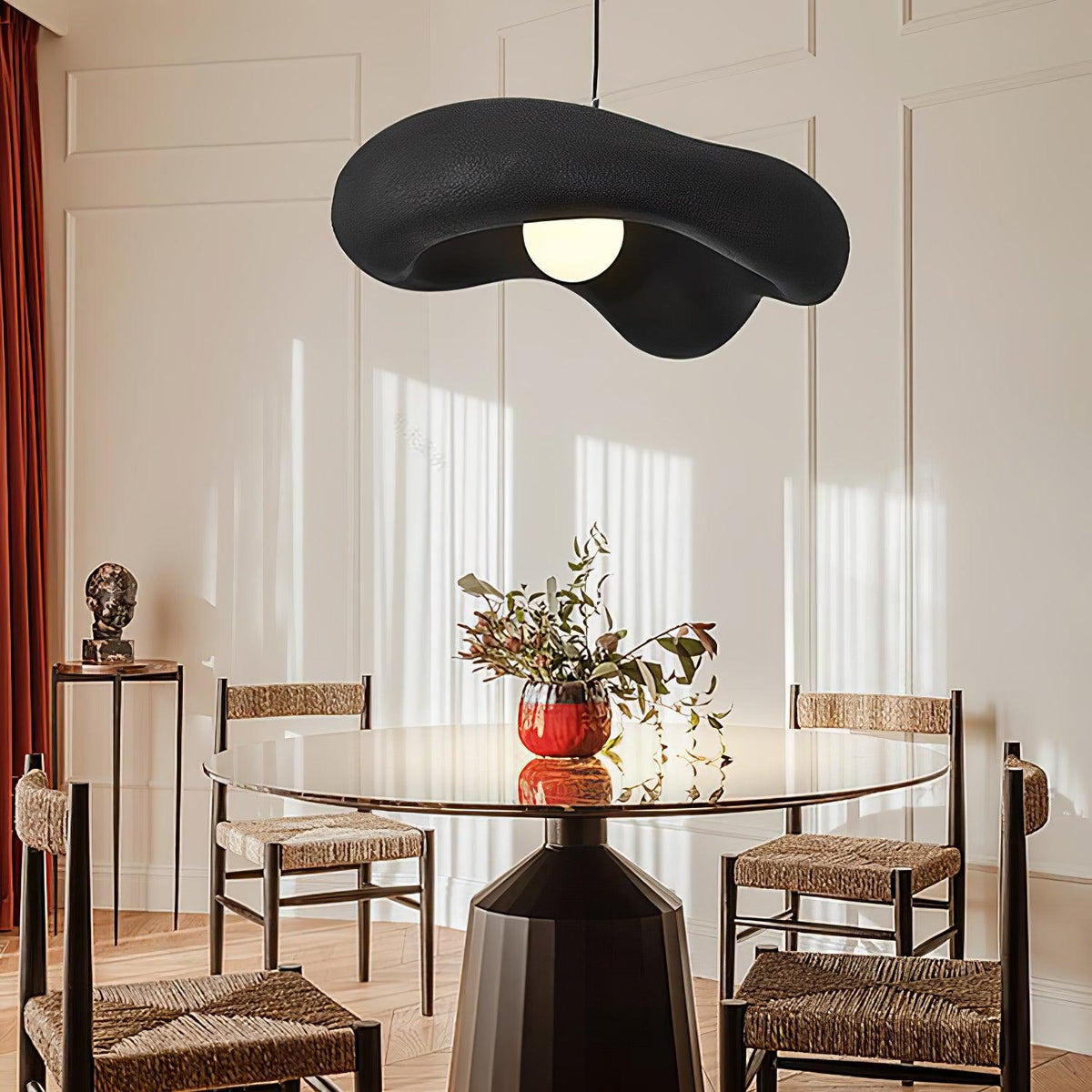 Black Clérachic pendant hung high in a panelled room, above a round glass table and rush-seat chairs.