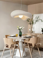 Beige Clérachic pendant over a round white pedestal table with wooden chairs, in a bright dining corner with a rattan sideboard.