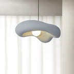 Grey Clérachic pendant with a rough, wavy shade and glowing bulb, hung in front of sheer white curtains.
