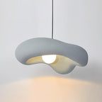 Grey Clérachic pendant lit against a pale wall, the pale blue-grey shade over a round bulb and a warm glow below.