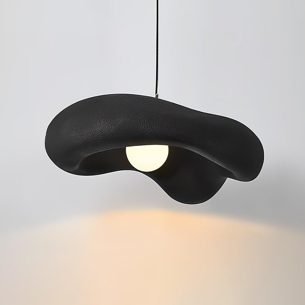 Black Clérachic pendant with a rough, wavy shade lit against a pale wall, a warm pool of light spreading below.
