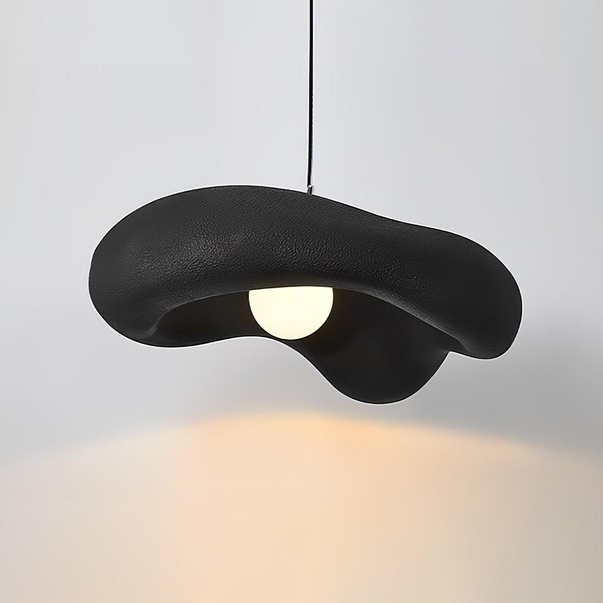 Black Clérachic pendant with a rough, wavy shade lit against a pale wall, a warm pool of light spreading below.