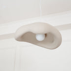 Beige Clérachic pendant seen from low down, with a round white bulb inside the folded shade, under a panelled white ceiling.