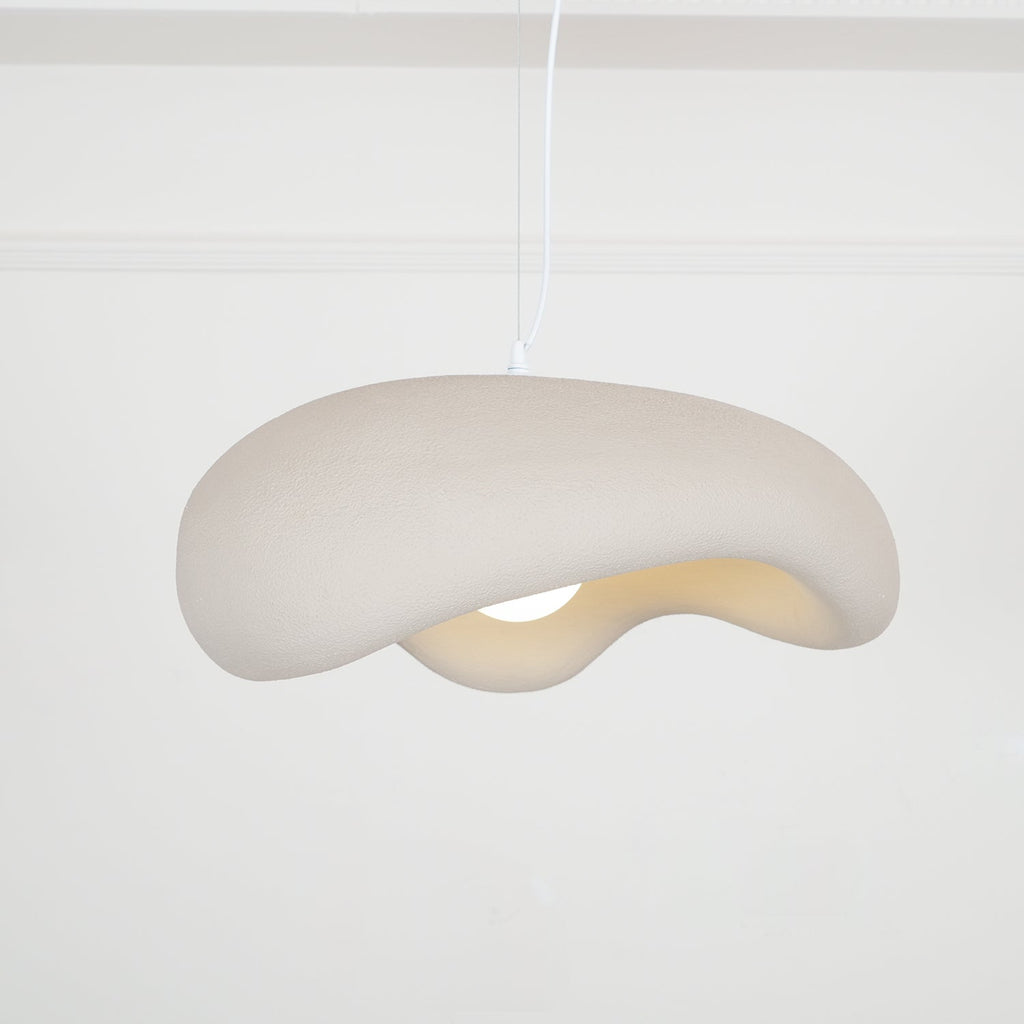Beige Clérachic pendant seen from below at an angle, its rough shade curling over a bulb, on a white cord against panelled walls.
