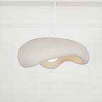 Beige Clérachic pendant seen from below at an angle, its rough shade curling over a bulb, on a white cord against panelled walls.