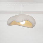 Beige Clérachic pendant hanging in front of a white panelled wall, the wavy shade showing a warm cream interior and a round bulb.