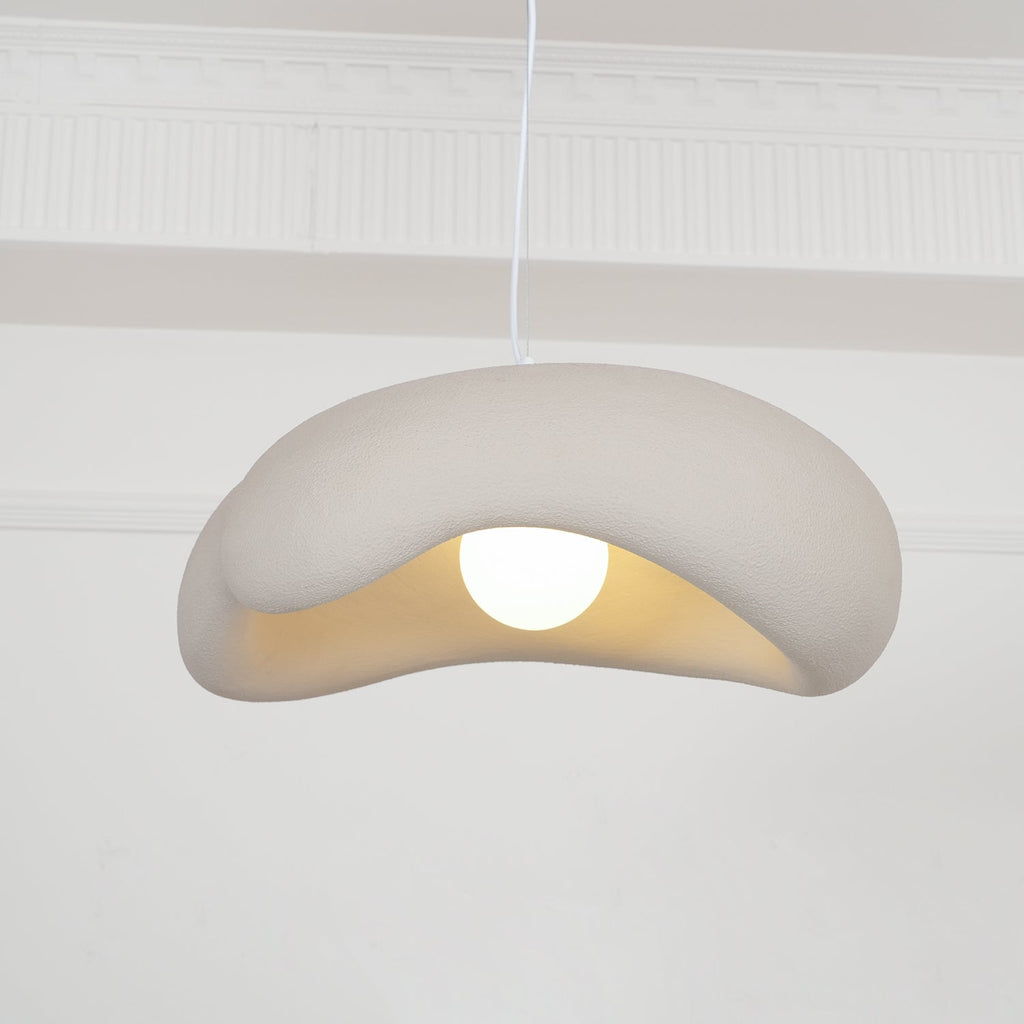 Beige Clérachic pendant with its rolled shade edge and a round bulb, in front of white wall mouldings.