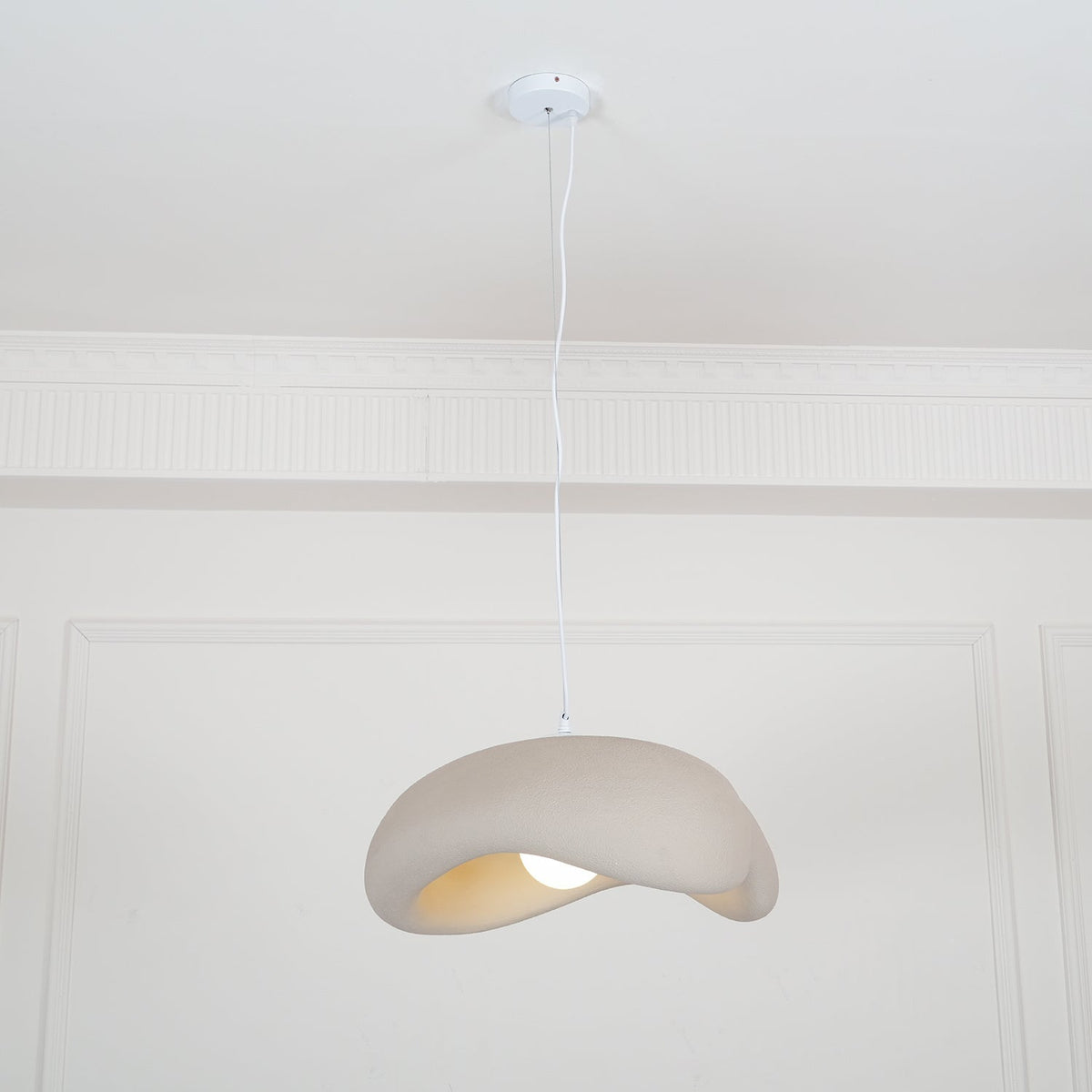 Beige Clérachic pendant on a white cord from a round white ceiling canopy, small in a tall panelled white room.
