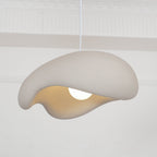 Beige Clérachic pendant tilted toward the camera, the thick folded shade and warm interior visible above a glowing bulb.