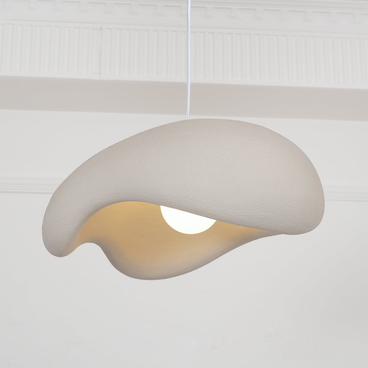 Beige Clérachic pendant tilted toward the camera, the thick folded shade and warm interior visible above a glowing bulb.