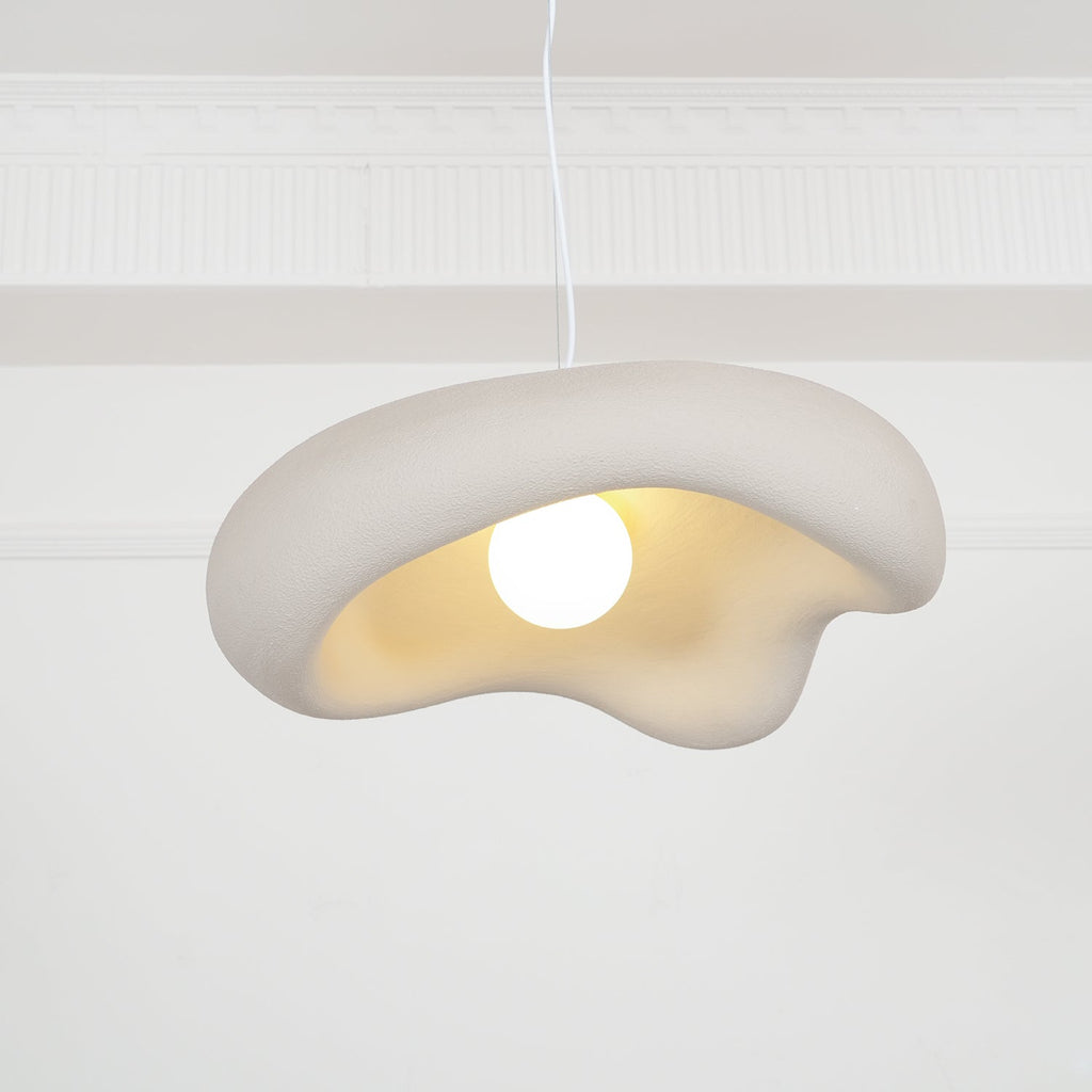 Beige Clérachic pendant with a lit bulb, the textured shade and cream underside close up against a white panelled wall.