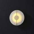 The Clérachic round wall lamp showing grey veining across the alabaster disc as light spills around the brass hub.