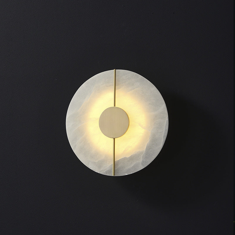 The Clérachic round wall lamp showing grey veining across the alabaster disc as light spills around the brass hub.