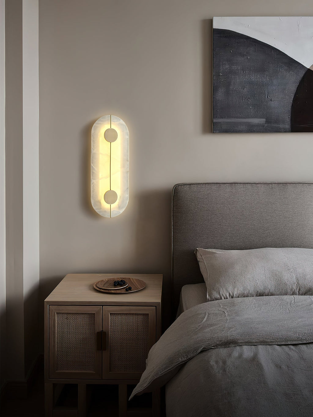 The Clérachic tall wall lamp glowing beside a bed, its alabaster face warm against a soft pale wall.
