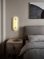 The Clérachic tall wall lamp glowing beside a bed, its alabaster face warm against a soft pale wall.