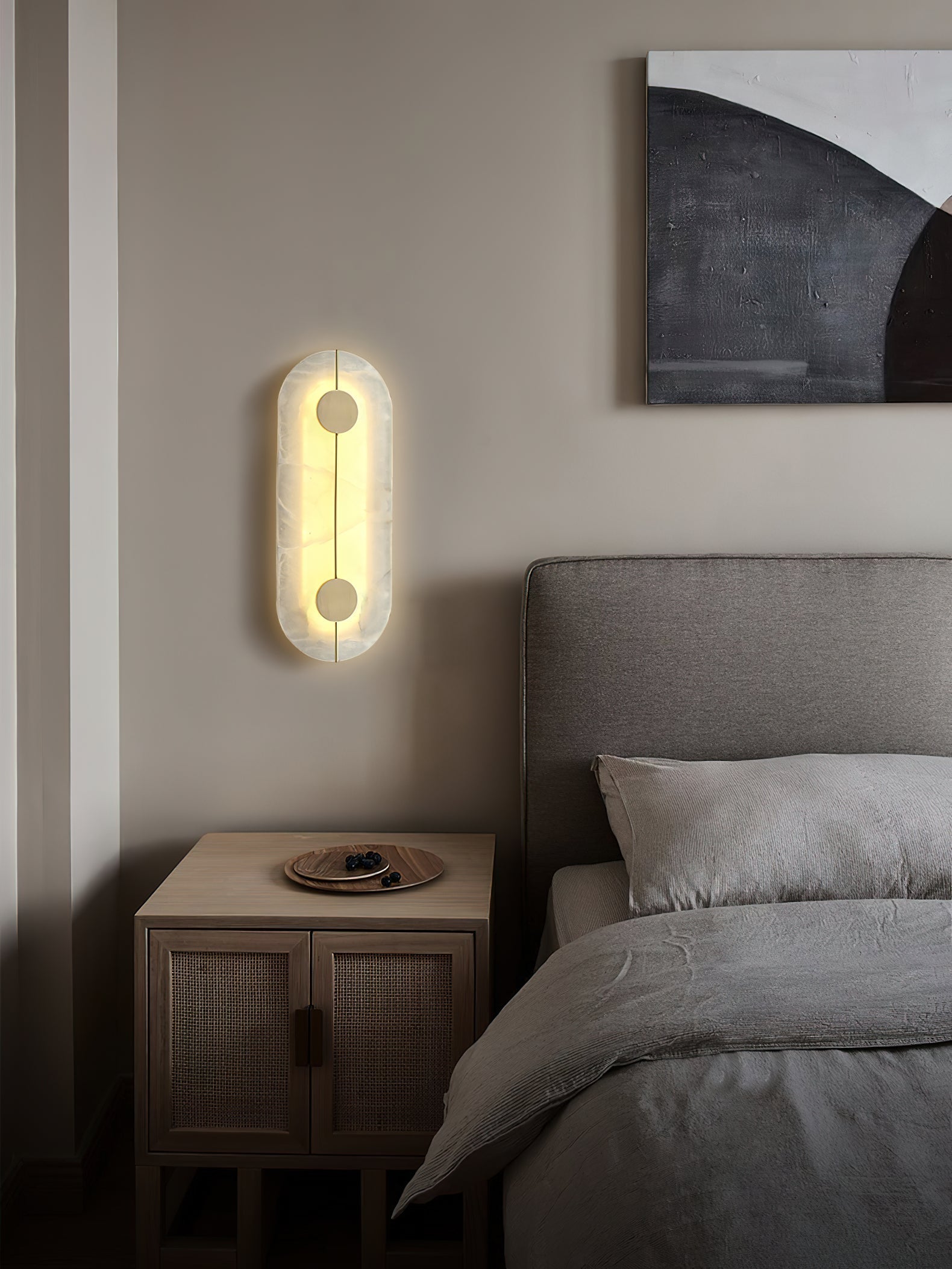 The Clérachic tall wall lamp glowing beside a bed, its alabaster face warm against a soft pale wall.