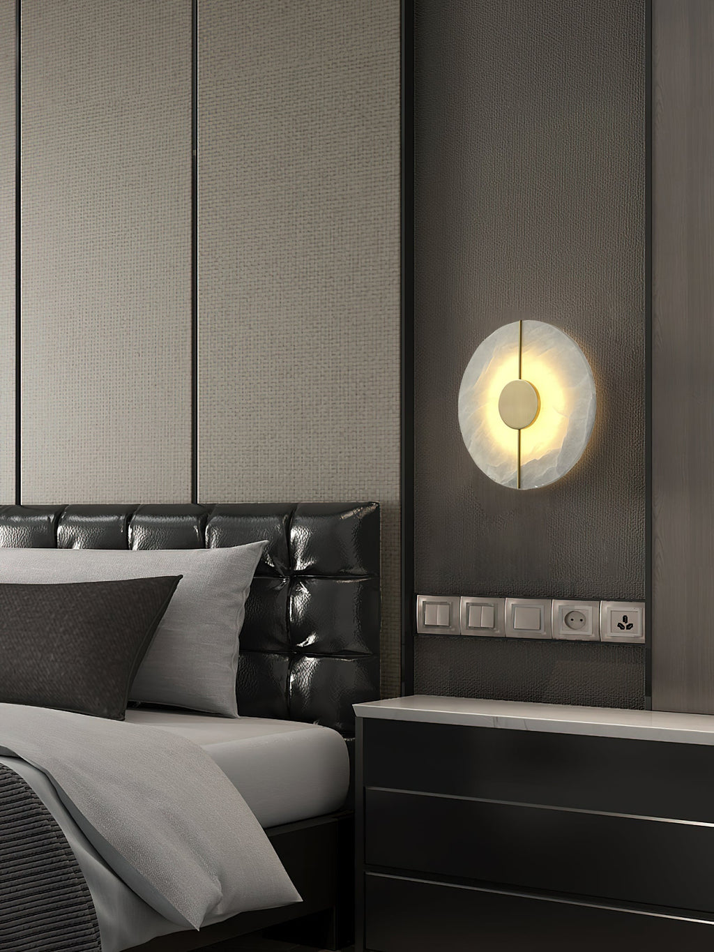 The Clérachic round wall lamp mounted above a black nightstand in a bedroom with a leather headboard.