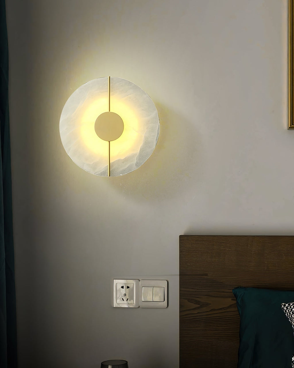 Clérachic round alabaster wall lamp casting a warm halo across the wall above a bed's headboard.