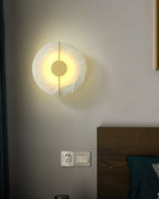 Clérachic round alabaster wall lamp casting a warm halo across the wall above a bed's headboard.