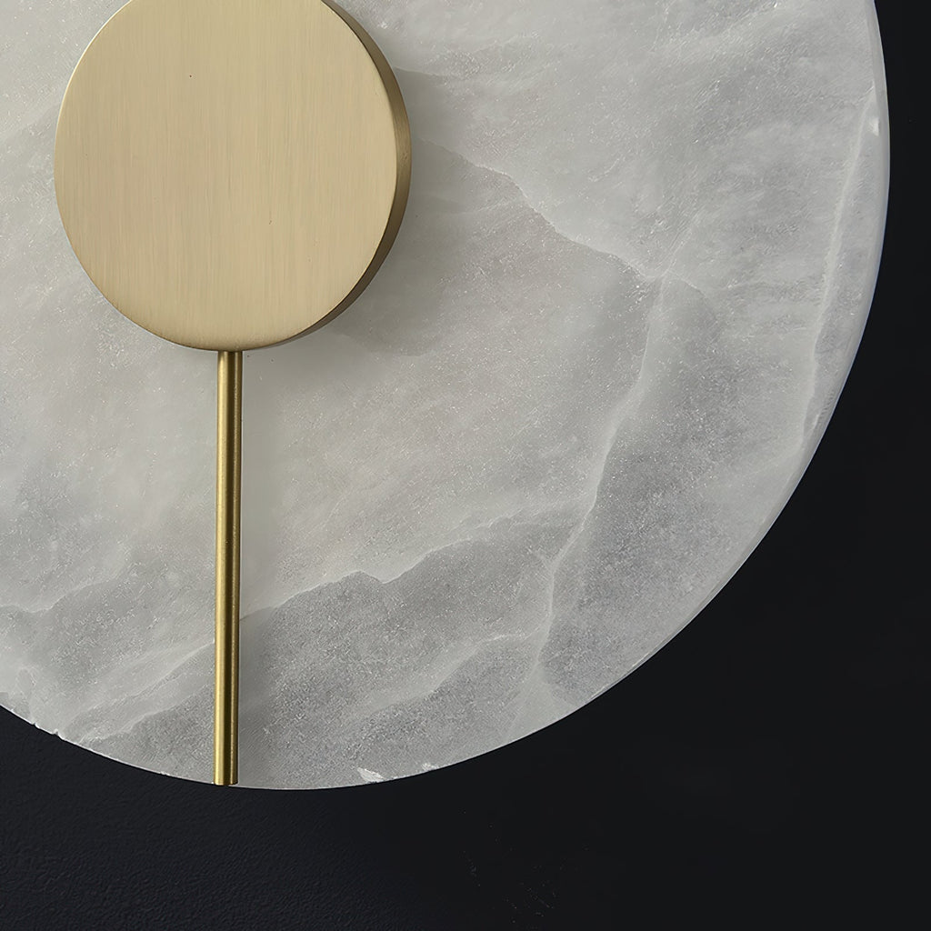 Clérachic wall lamp close-up: brushed brass disc and slim rod set against the pale, cloudy alabaster face.