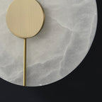 Clérachic wall lamp close-up: brushed brass disc and slim rod set against the pale, cloudy alabaster face.