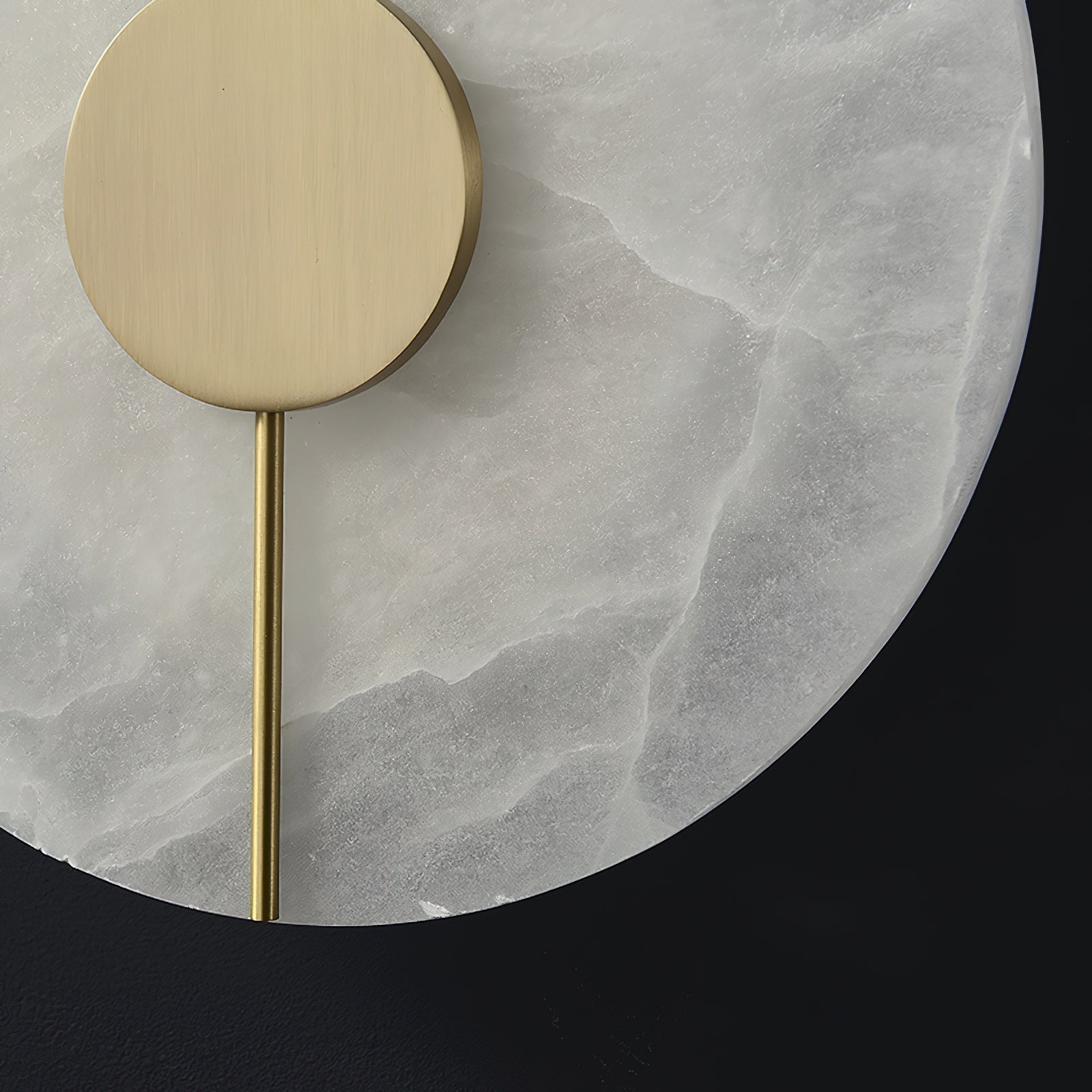 Clérachic wall lamp close-up: brushed brass disc and slim rod set against the pale, cloudy alabaster face.
