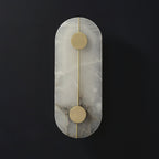 The Clérachic tall capsule wall lamp unlit on a dark wall, grey veining marbling the alabaster slab.