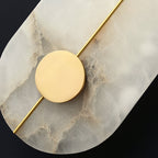 Clérachic wall lamp detail: a brass rod crossing the brass disc over deeply veined alabaster, seen up close.