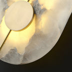 The Clérachic wall lamp seen close while lit, amber glow rising through the translucent alabaster stone.