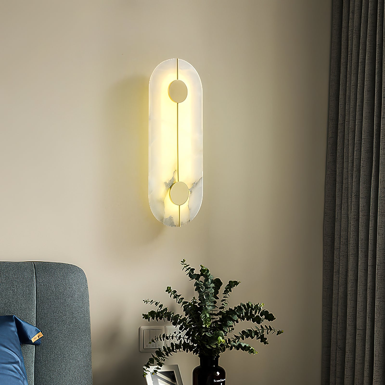 The Clérachic tall wall lamp lit beside a blue upholstered headboard, curtain and eucalyptus sprigs alongside.