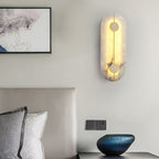 The Clérachic tall alabaster sconce glowing above a bed ledge, a blue vessel and framed print beside it.