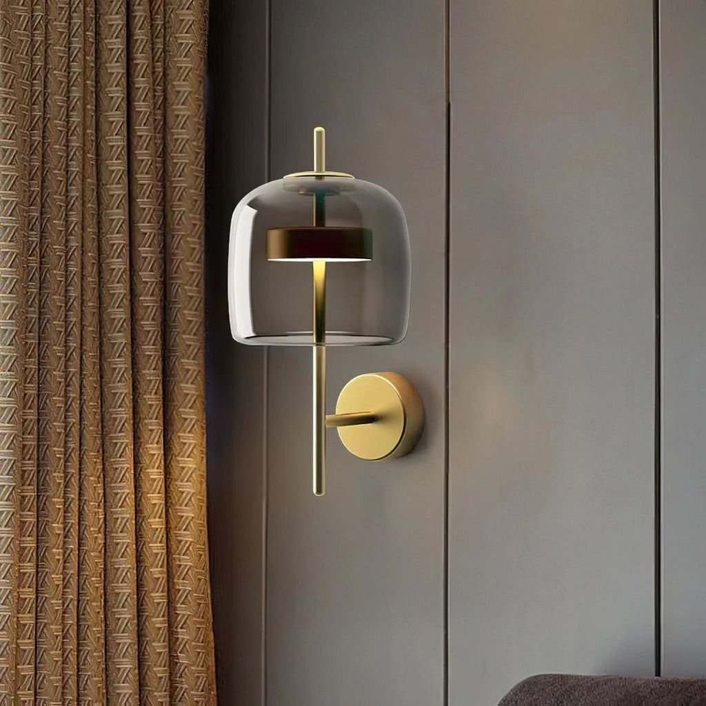 A Gold & Smoke Grey Clérachic wall light on a grey panelled wall beside a gold woven curtain, with a soft glow inside the shade.