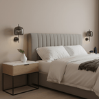 Black and smoke grey Clérachic wall lights sit either side of a grey upholstered bed, with a white marble-top bedside table below.