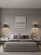 Two black Clérachic wall lights with smoke grey shades glow above white bedside tables, either side of a framed print and a bed.