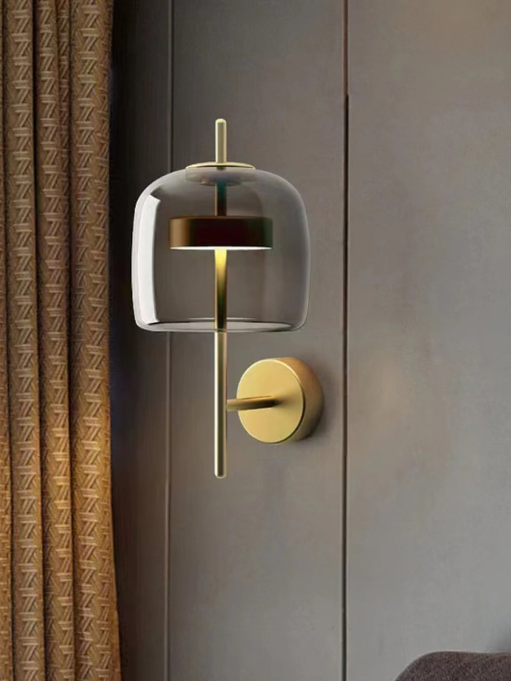 Gold & Smoke Grey Clérachic wall light on a grey wall, with a smoked glass shade, a lit gold stem and a woven curtain at the edge.