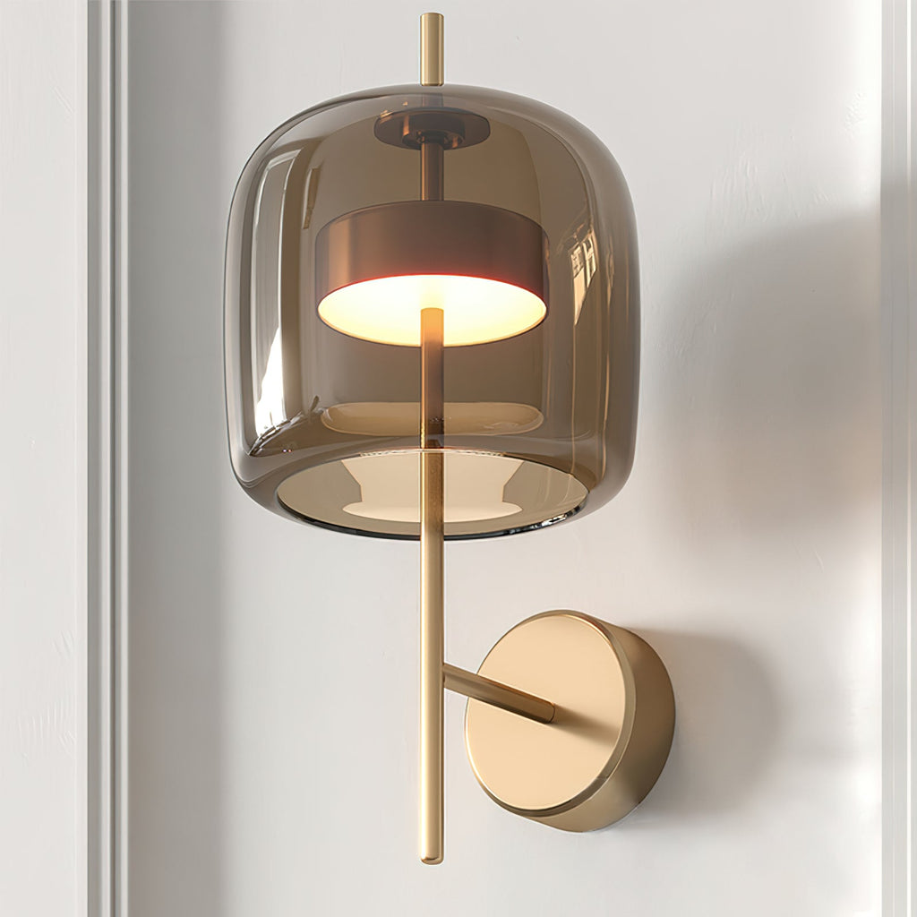 Close view of the lit smoke grey glass shade, gold stem and round backplate of this Clérachic wall light on a pale wall.