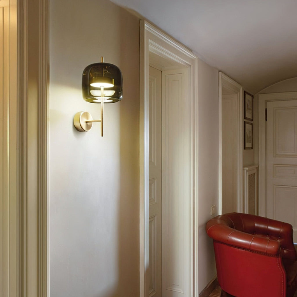 This Clérachic wall light glows warm on the wall of a hallway with white doors, above a red leather armchair.