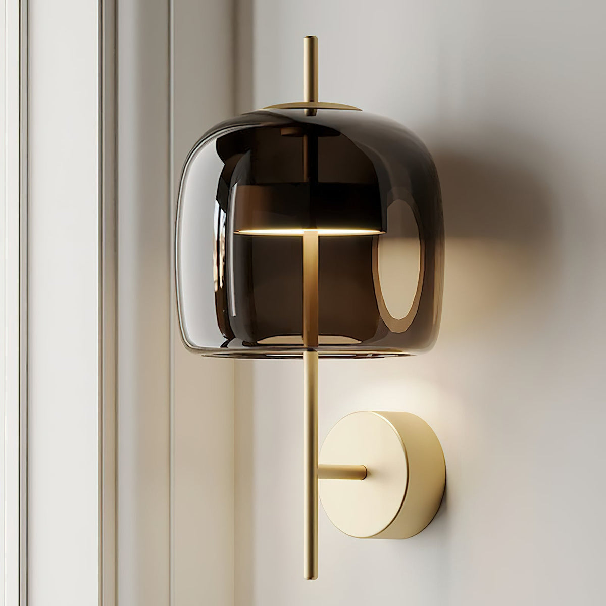 Close view of a smoke grey glass shade lit from inside, with a gold stem and gold backplate, on this Clérachic wall light.