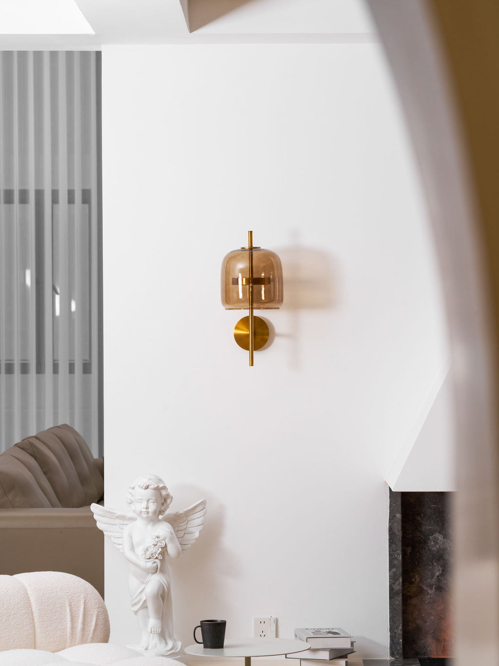 This Clérachic wall light in gold and coffee glass, seen from further back on a white wall by an arched opening and a cherub statue.